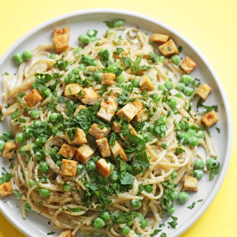 En tallerken med kremet vegansk pasta carbonara tofu, ferske urter og grønne erter.