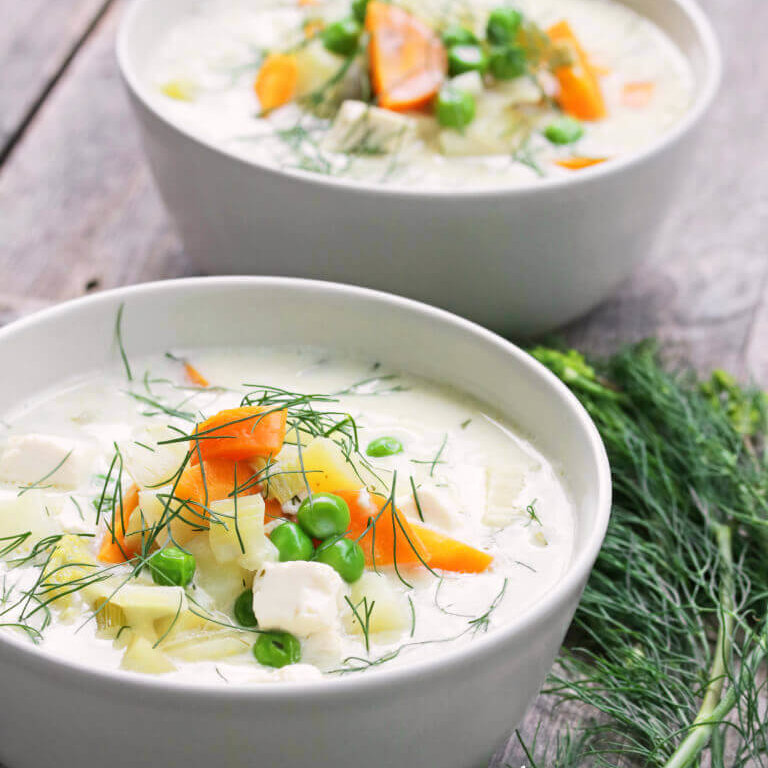 Fersk dill drysset over en kremet, vegansk fiskesuppe med grønnsaker i en dyp skål.