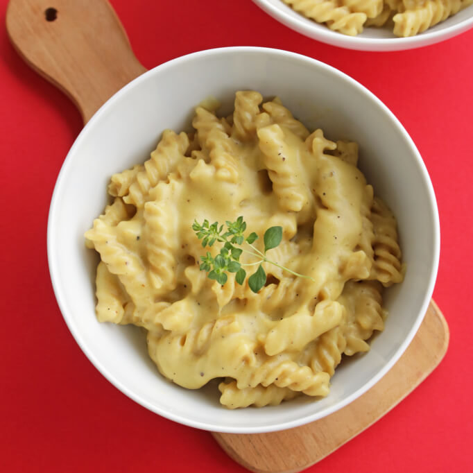 En skål med kremete vegansk mac and cheese, pyntet med en frisk oreganokvist.