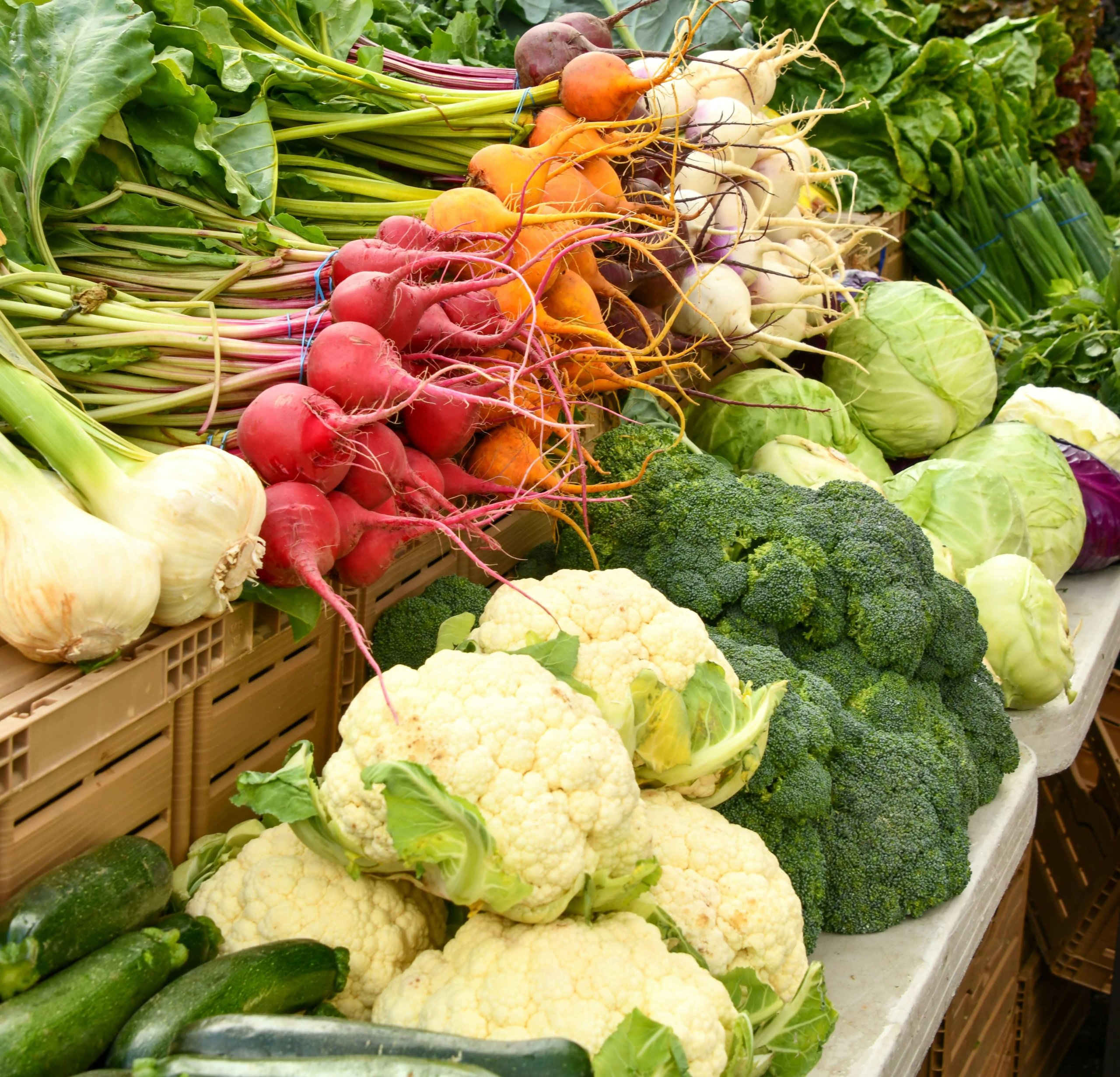 flere hvitløk, reddik, squash, blomkål, brokkoli og kålhoder ligger på hyller i en grønnsakshandel