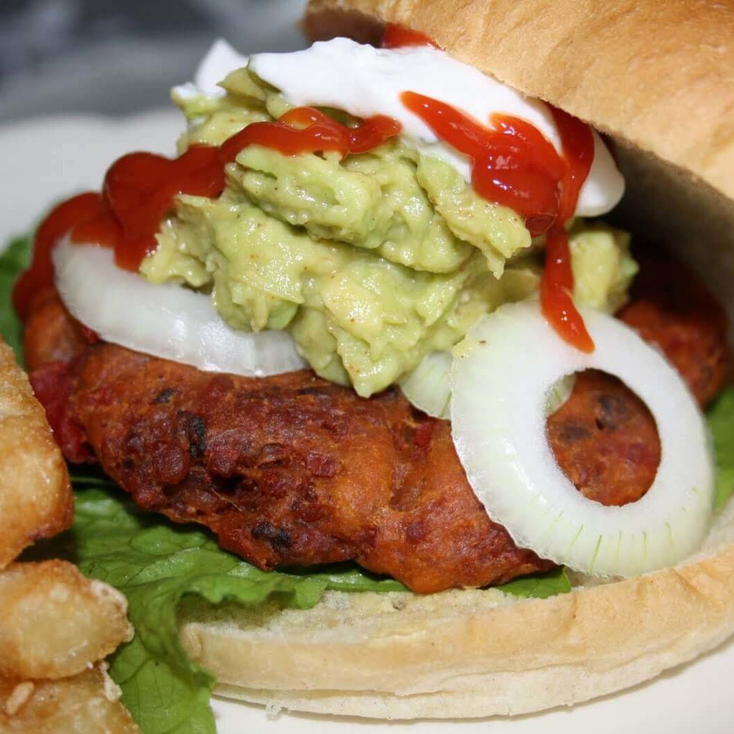 Vegansk baconburger med avokadofyll ligger mellom to luftige burgerbrød, frisk salat, løk og dressing.