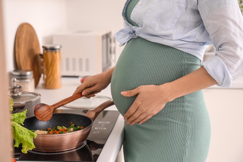 en gravid kvinne holder på magen sin mens hun lager mat