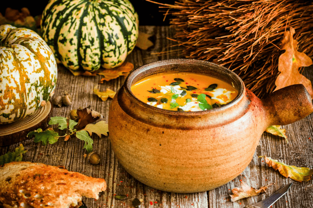 Gresskarsuppe i en terracotta skål med løv og gresskar på bordet rundt