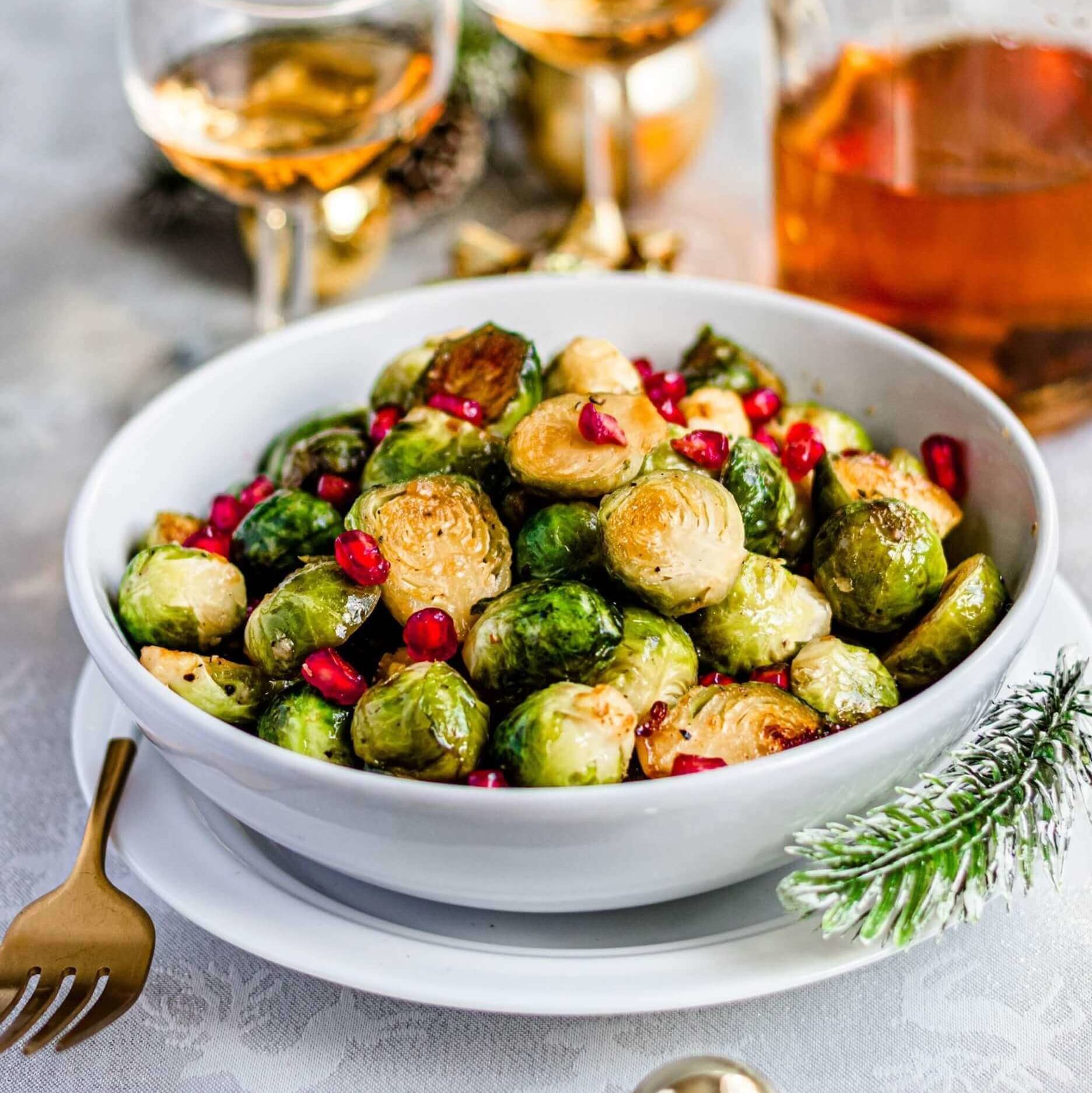 En skål med stekt rosenkål, toppet med granateplekjerner står på et dekket julebord.