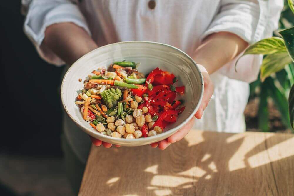 Hender som holder en bolle med salat som inneholder belgfrukter