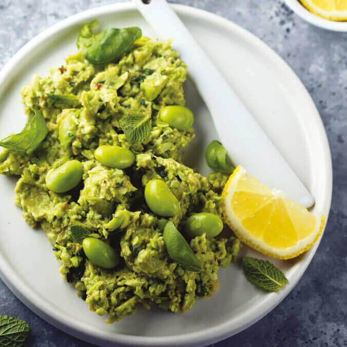 Toast genereøst toppet med edamame og chili guacamole. Akkompagnert med en skive sitron ved siden av.