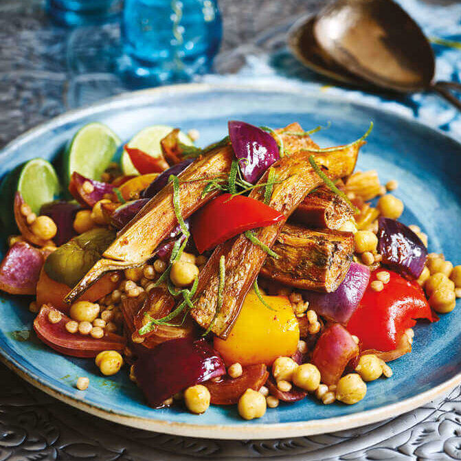 Bakt aubergine-couscous toppet med revet limeskall på en blå keramikktallerken.