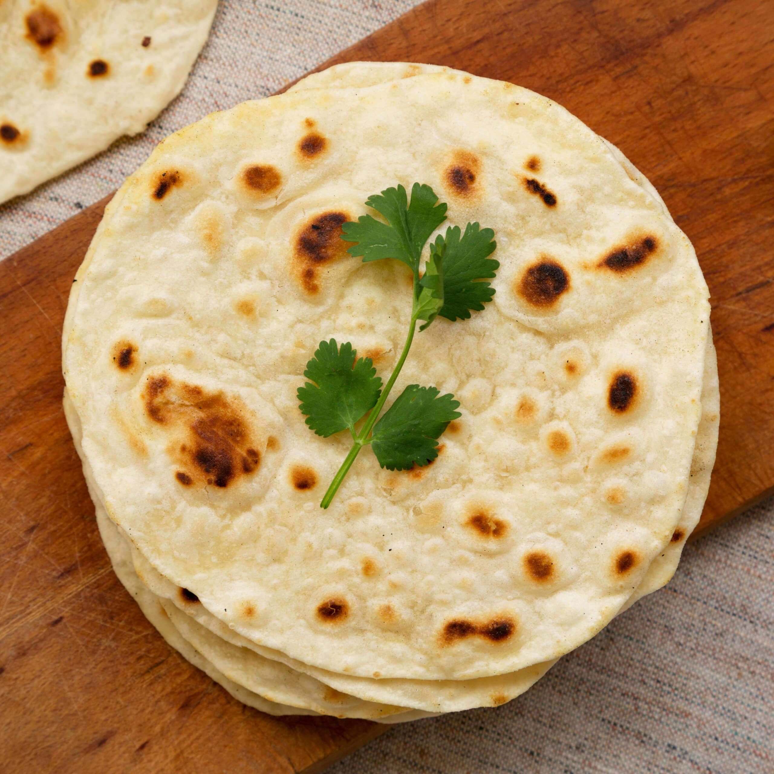 Nybakte runde chapati-brød med et ferskt korianderblad til pynt.