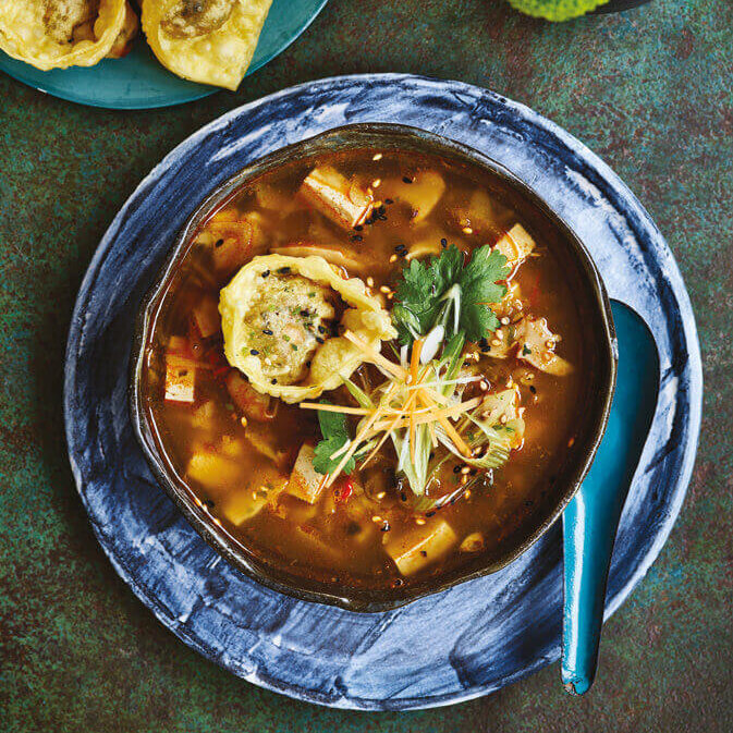 En skål med sterk og syrlig suppe, toppet med sprø wonton-dumplings og frisk garnityr.