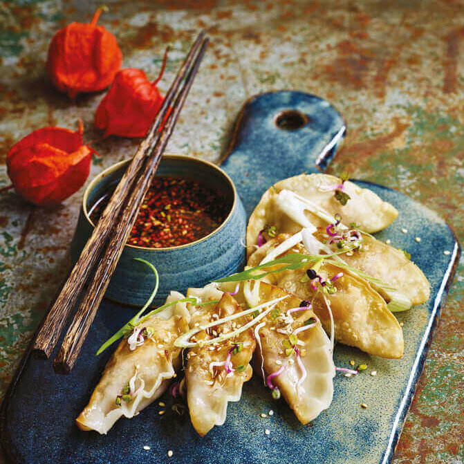 Et flatt keramikkbrett med nylagde gyozas toppet med grønn garnityr.