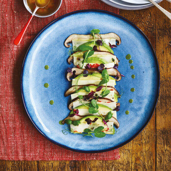 Brokkolicarpaccio med avokado ligger flott dandert på en blå keramikktallerken.