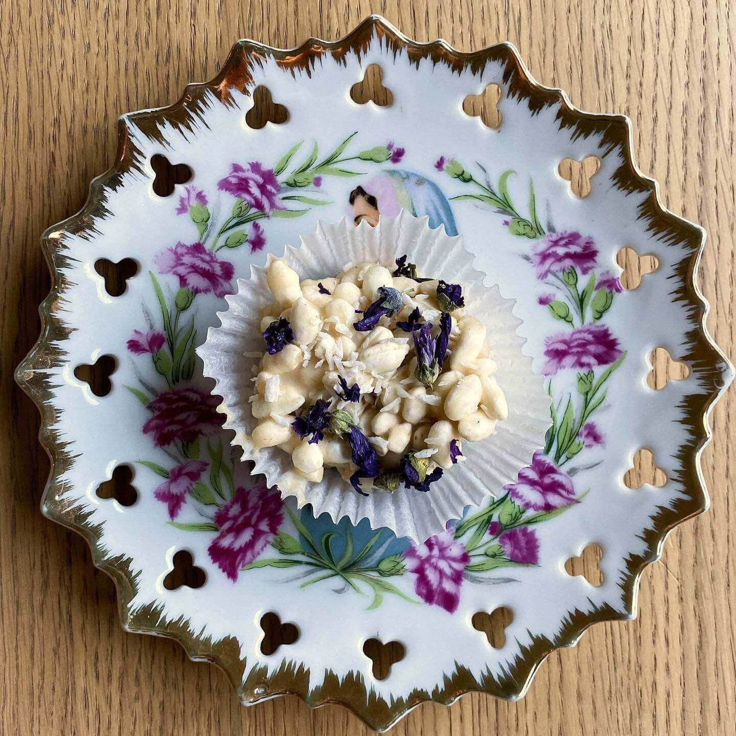 En hvit risbolle med hvit sjokolade ligger på et porselensfat med blomsterdetaljer.