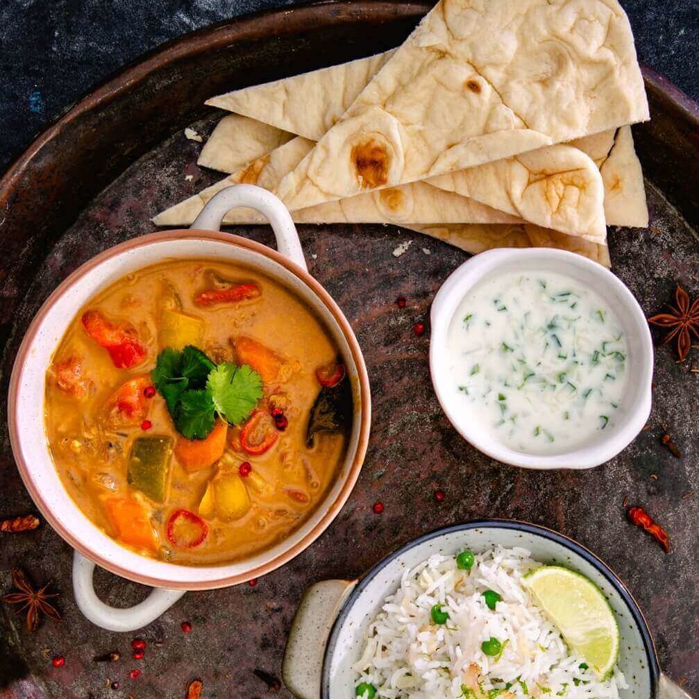 Oransje massaman curry-gryte med tynne brød, ris og dipp.