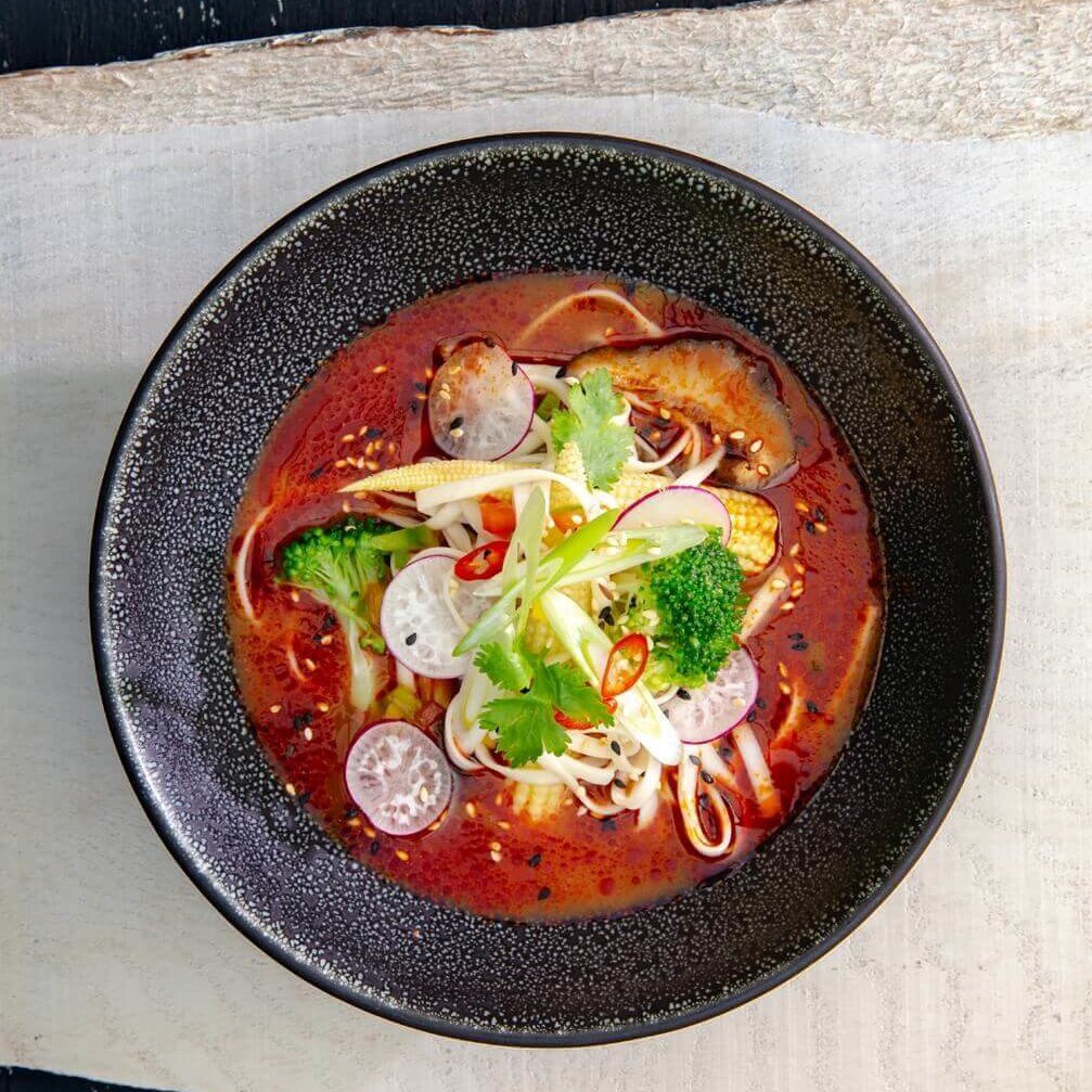 En keramikkskål med fargesterk tom yum-suppe, toppet med sesamfrø.