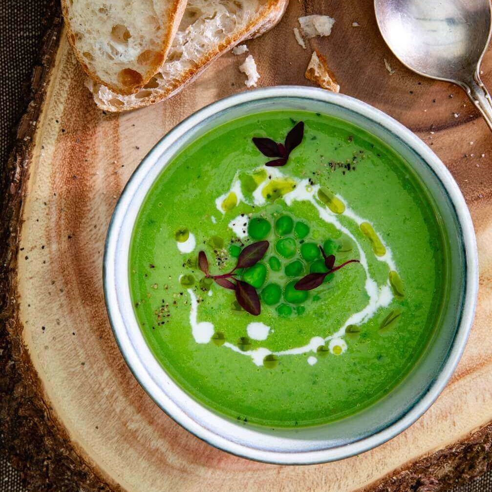 En skål grønn ertesuppe med topping og en skvett trøffelolje plassert på ei trefjøl.