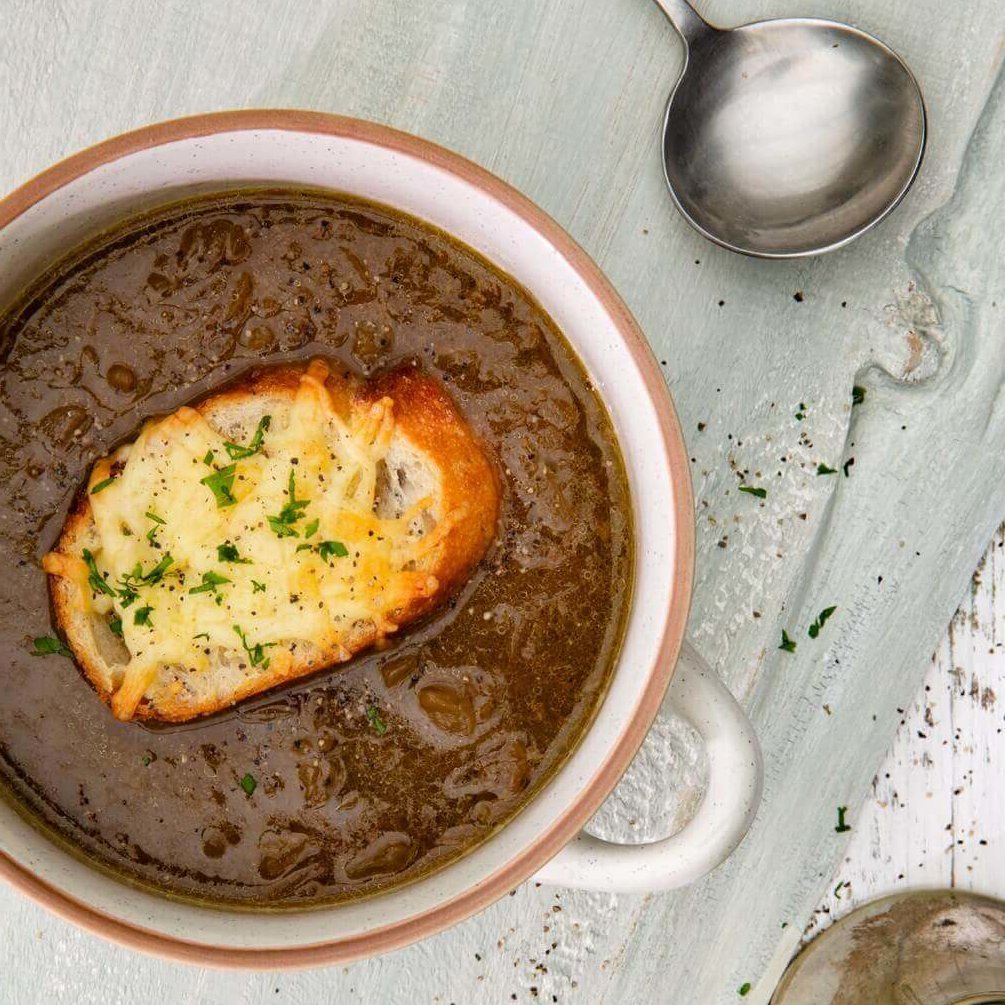 En rustikk skål fransk løksuppe med en sprø, ostetoppet skive med brød.