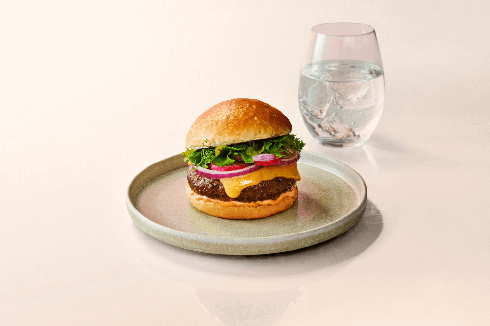 En kultivert burger fra mosa meat ved siden av et vannglass.