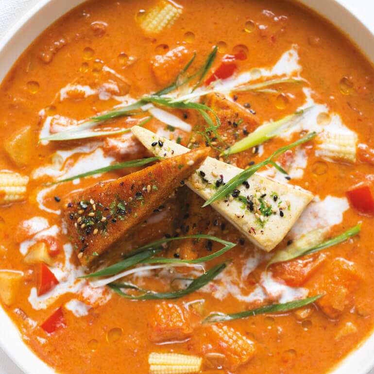 En skål varm, oransjefarget curry med tofu og grønnsaker.
