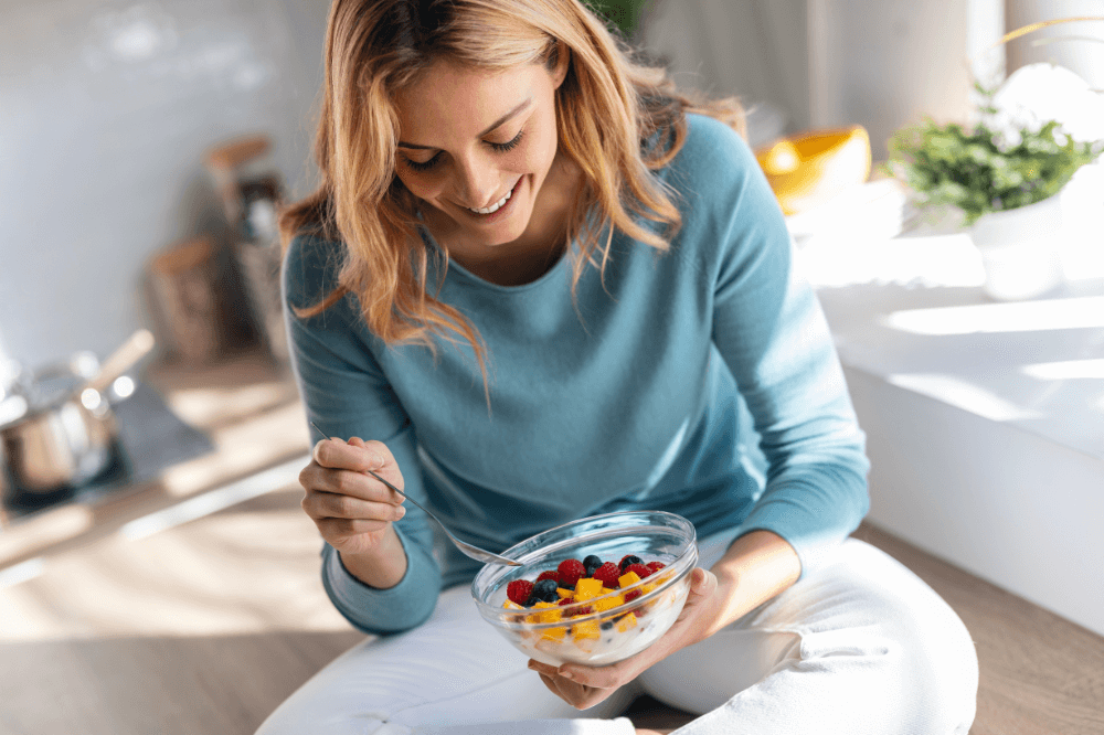 Kvinne spiser en sunn skål med fruktsalat.