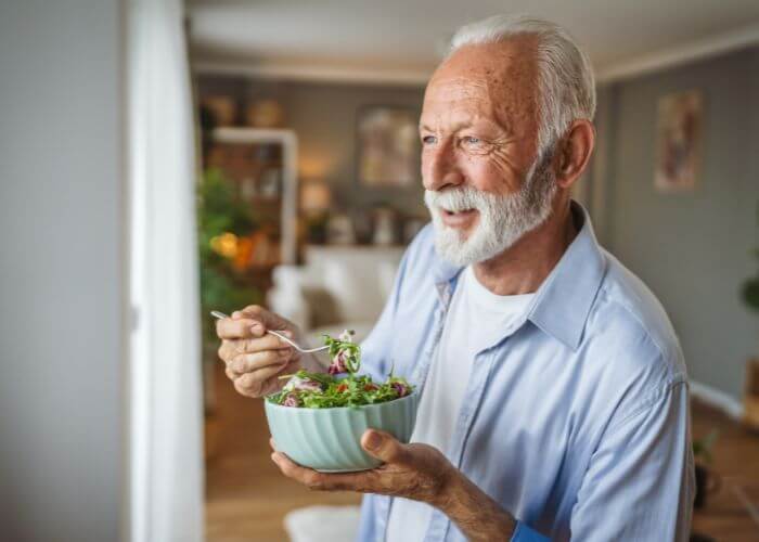 Eldre mann som spiser en skål med salat.