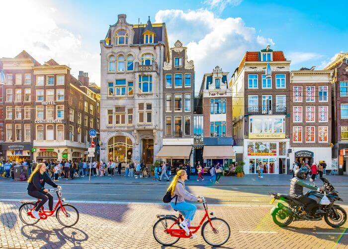 Bilde av klassiske Amsterdam by-hus, med mennesker som sykler i forgrunnen.