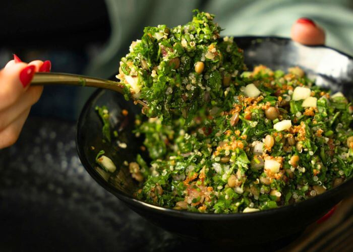 Salat med grønnkål, pinjekjerner, og byggryn i en mørk skål. 