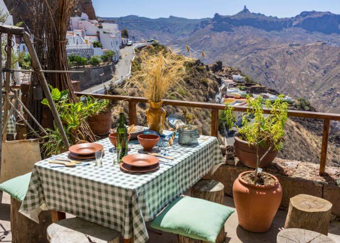 Uteservering på en restaurant i fjellsiden på Gran Canaria. Bordet er dekket med rutet duk og service. 