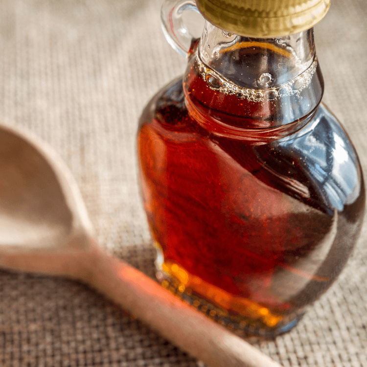 En flaske lønnesirup står på et bord ved siden av en treskje.