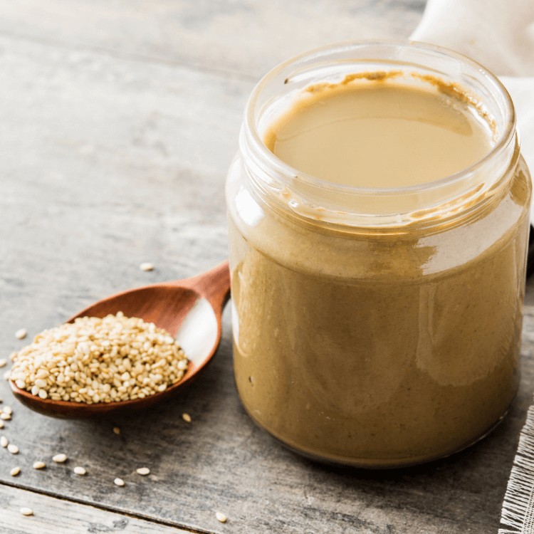 Et glass med tahini ved siden av en skje med sesamfrø.
