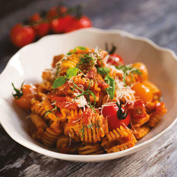 en skål radiatoripasta med rød tomatsaus og cherrytomater.