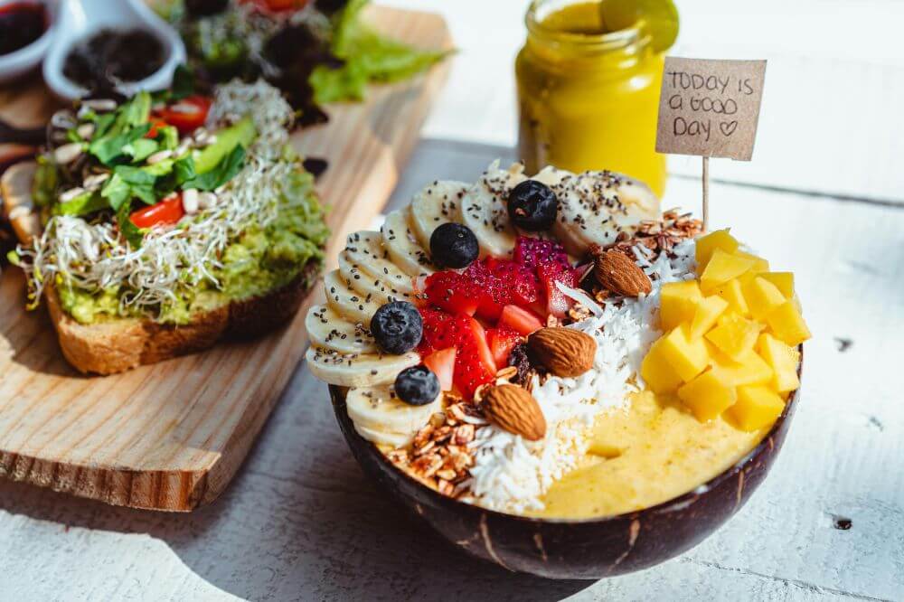 Frokost med avokado-toast og en smoothie bowl toppet med frukt og bær.