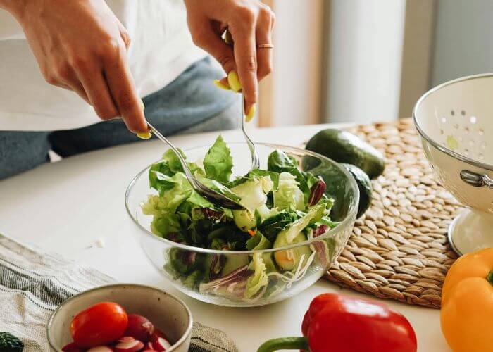 Ung kvinne som blander en salat i glasskål. 